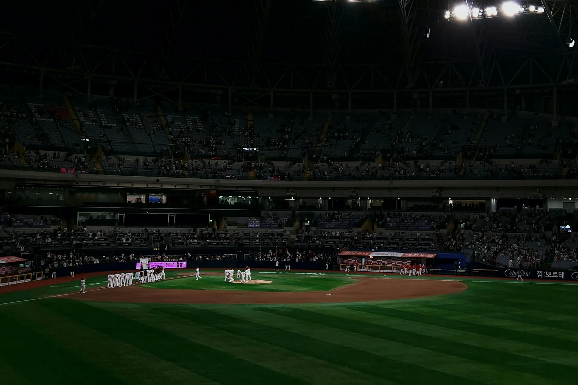 En KBO-baseballkamp i gang om aftenen i et fyldt sydkoreansk stadion, flomlys der blænder over infieldet, og spillere samlet ved mounden